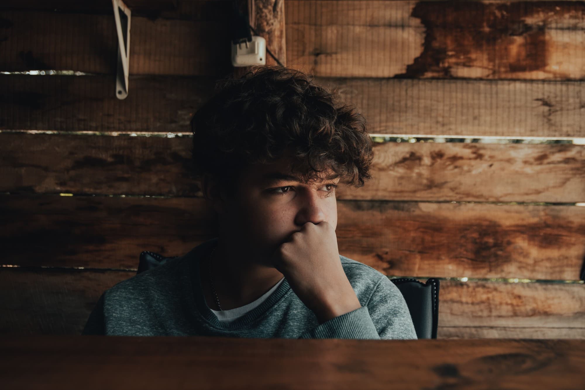 A thoughtful teenager sitting quietly at a wooden table